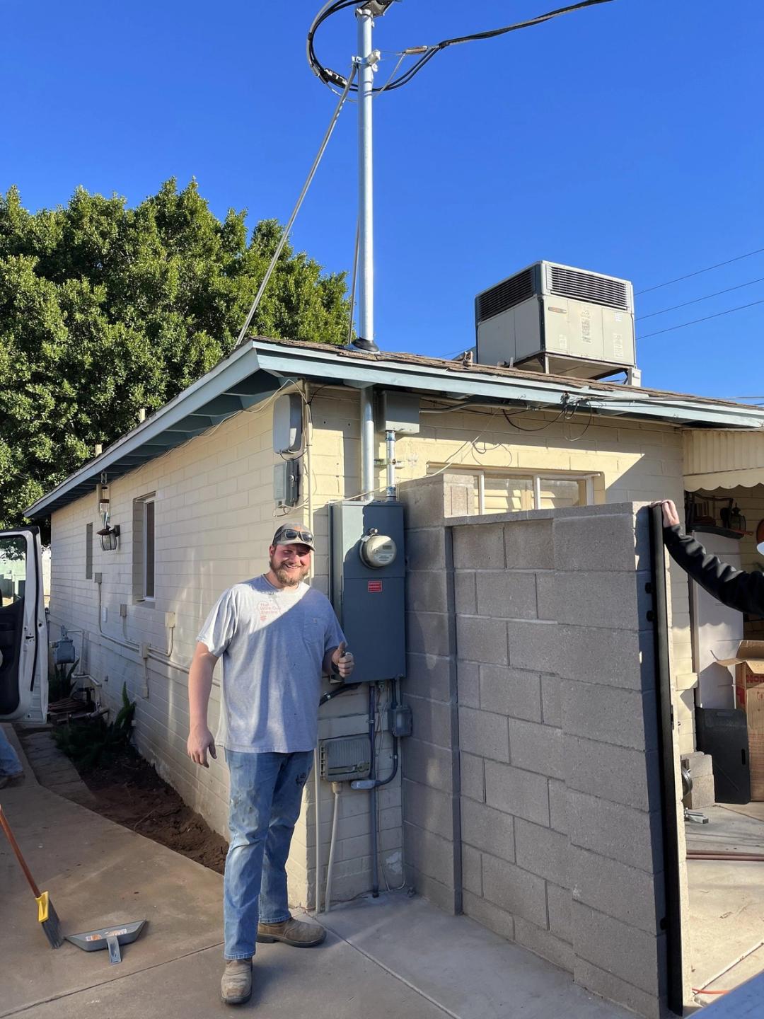 Electrician giving a thumbs up beside a new meter panel and service mast on a home