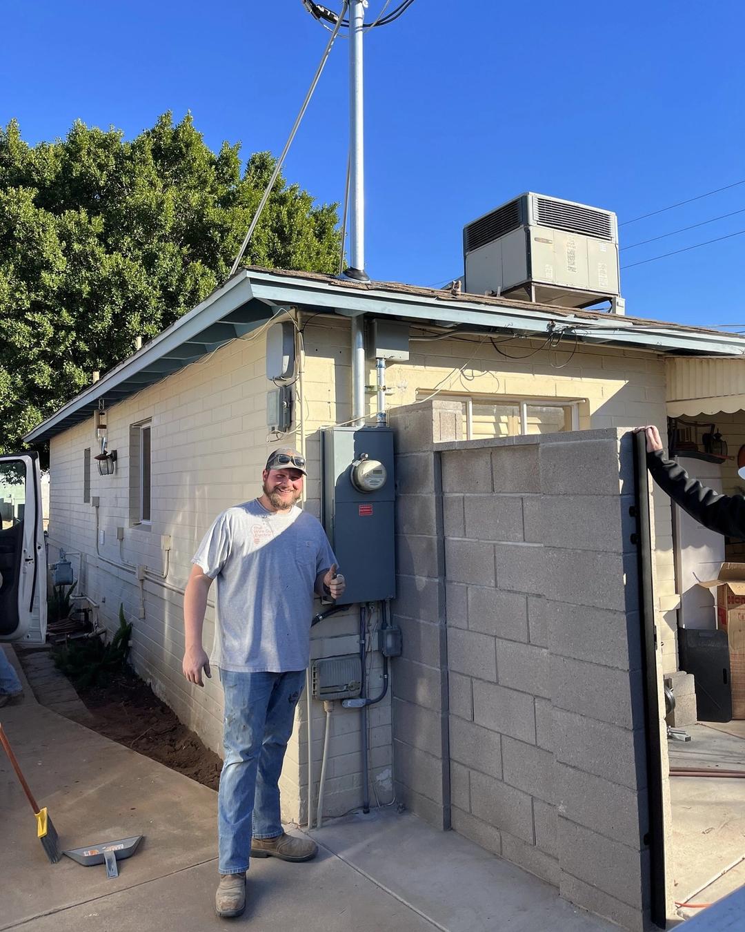Electrician giving a thumbs up beside a new meter panel and service mast on a home