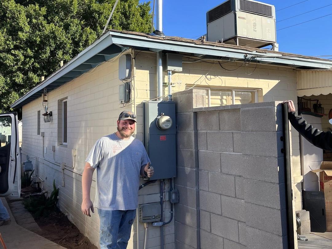 Electrician giving a thumbs up beside a new meter panel and service mast on a home