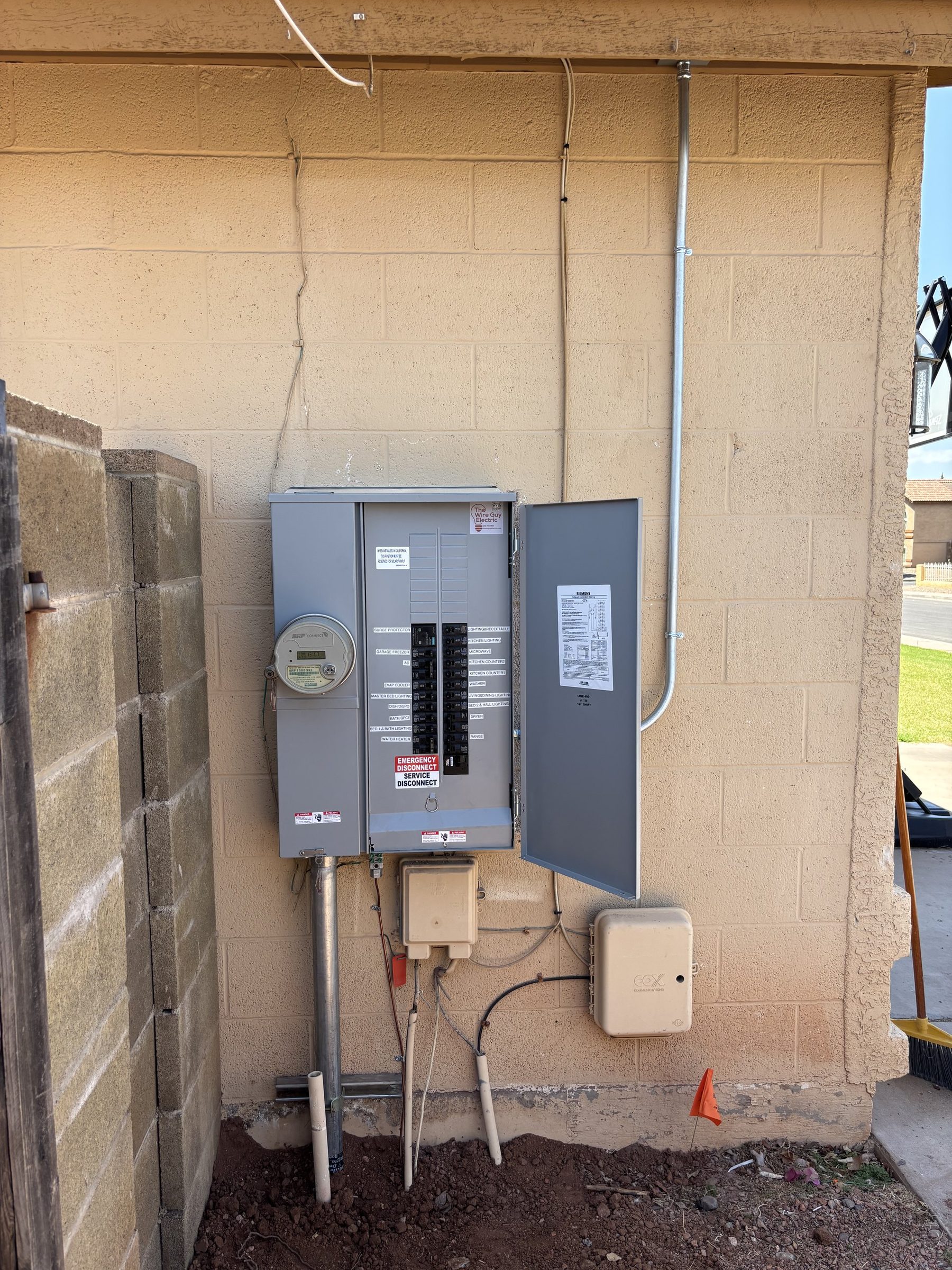 New meter and breaker panel combo mounted on a tan block wall with fresh conduit