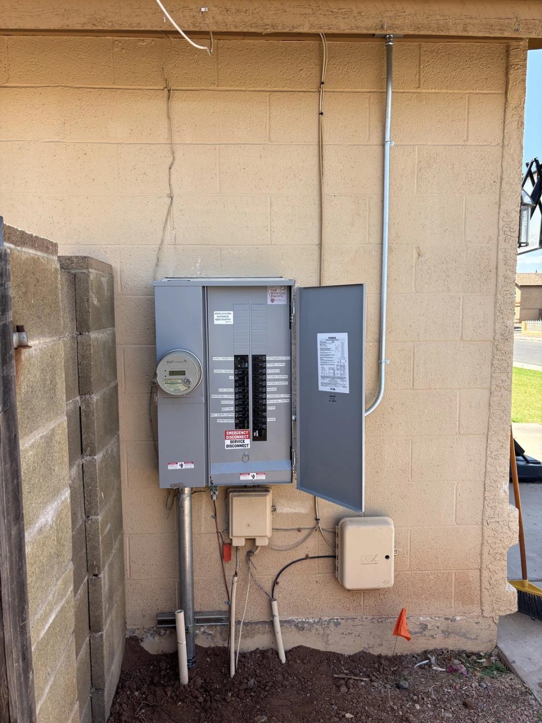 New meter and breaker panel combo mounted on a tan block wall with fresh conduit