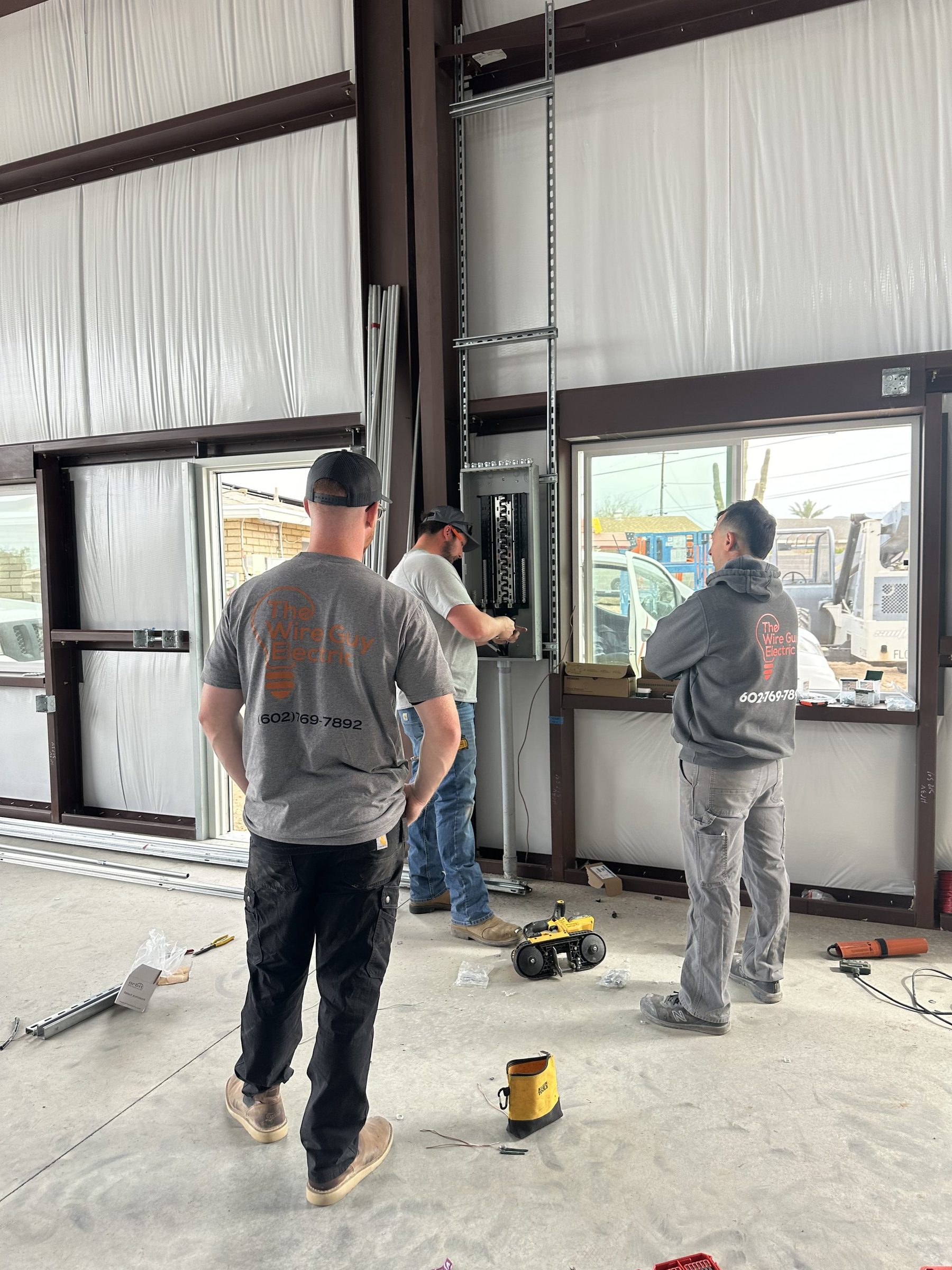 Three electricians working on a new panel inside a metal commercial building