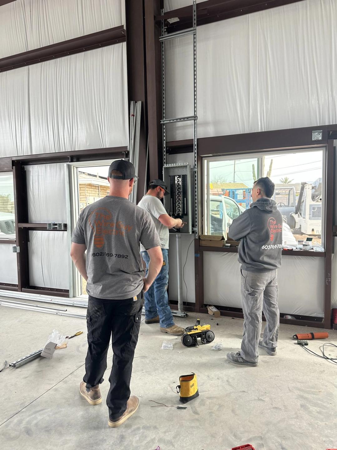 Three electricians working on a new panel inside a metal commercial building