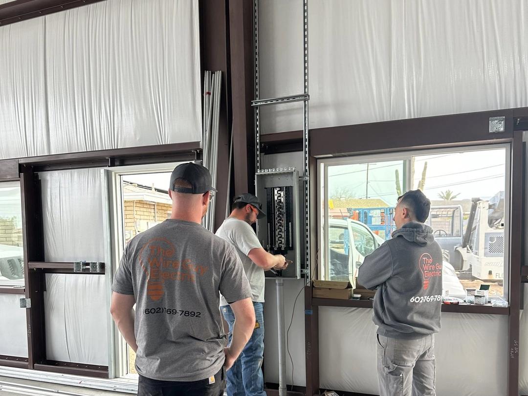 Three electricians working on a new panel inside a metal commercial building