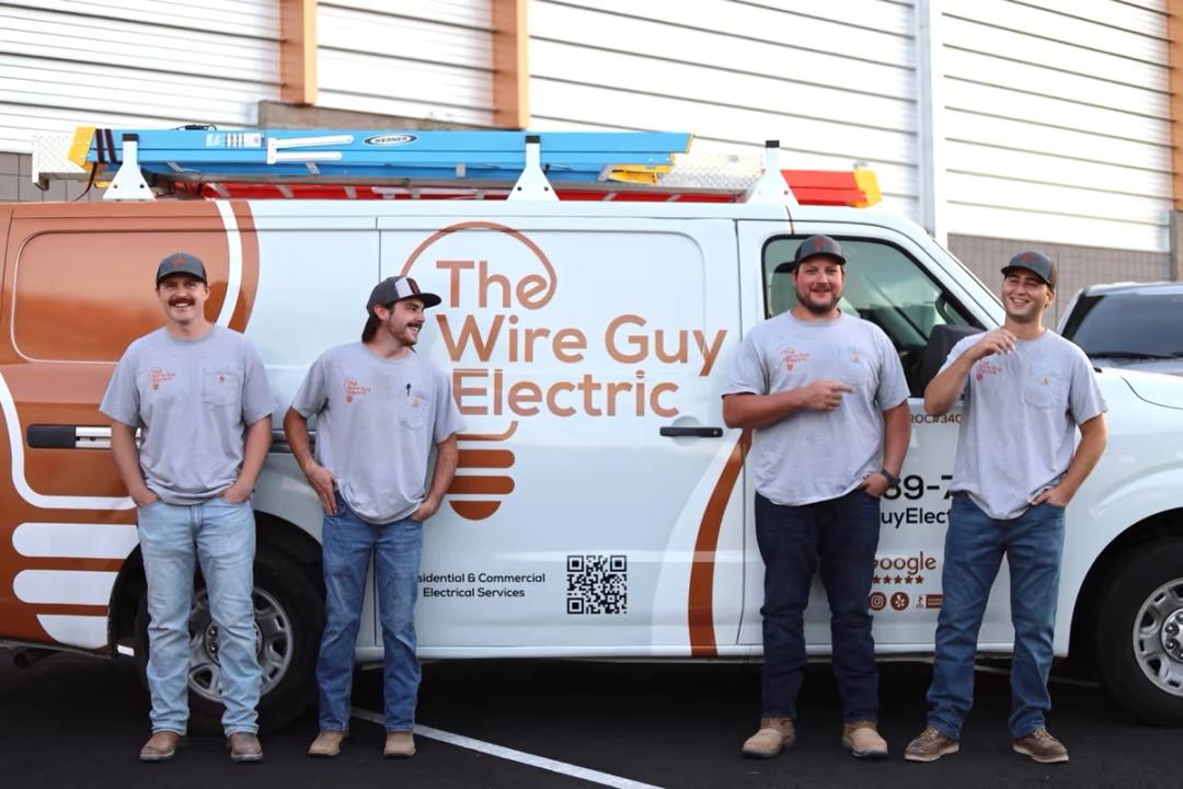 Four Wire Guy Electric technicians in front of a company van wrapped with the logo, one of them pointing at it
