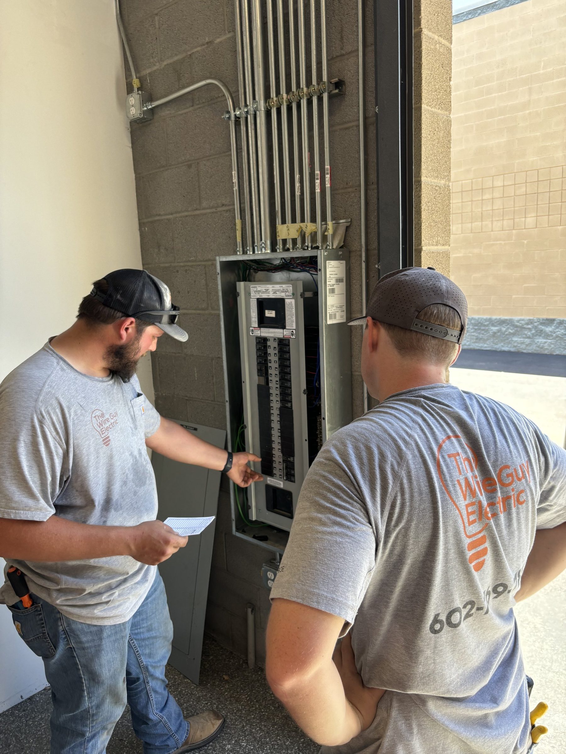 Two Wire Guy Electric electricians reviewing a commercial panel fed by multiple conduits