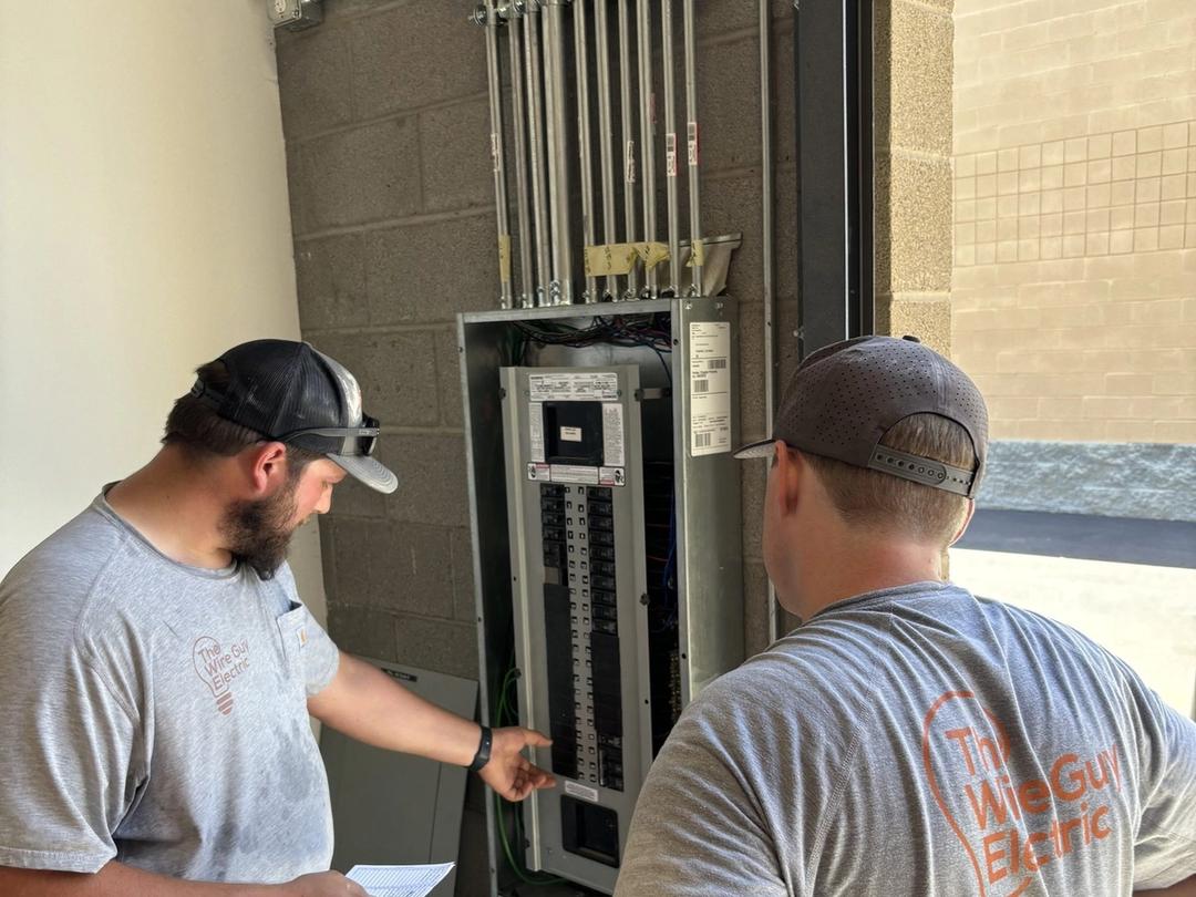 Two Wire Guy Electric electricians reviewing a commercial panel fed by multiple conduits