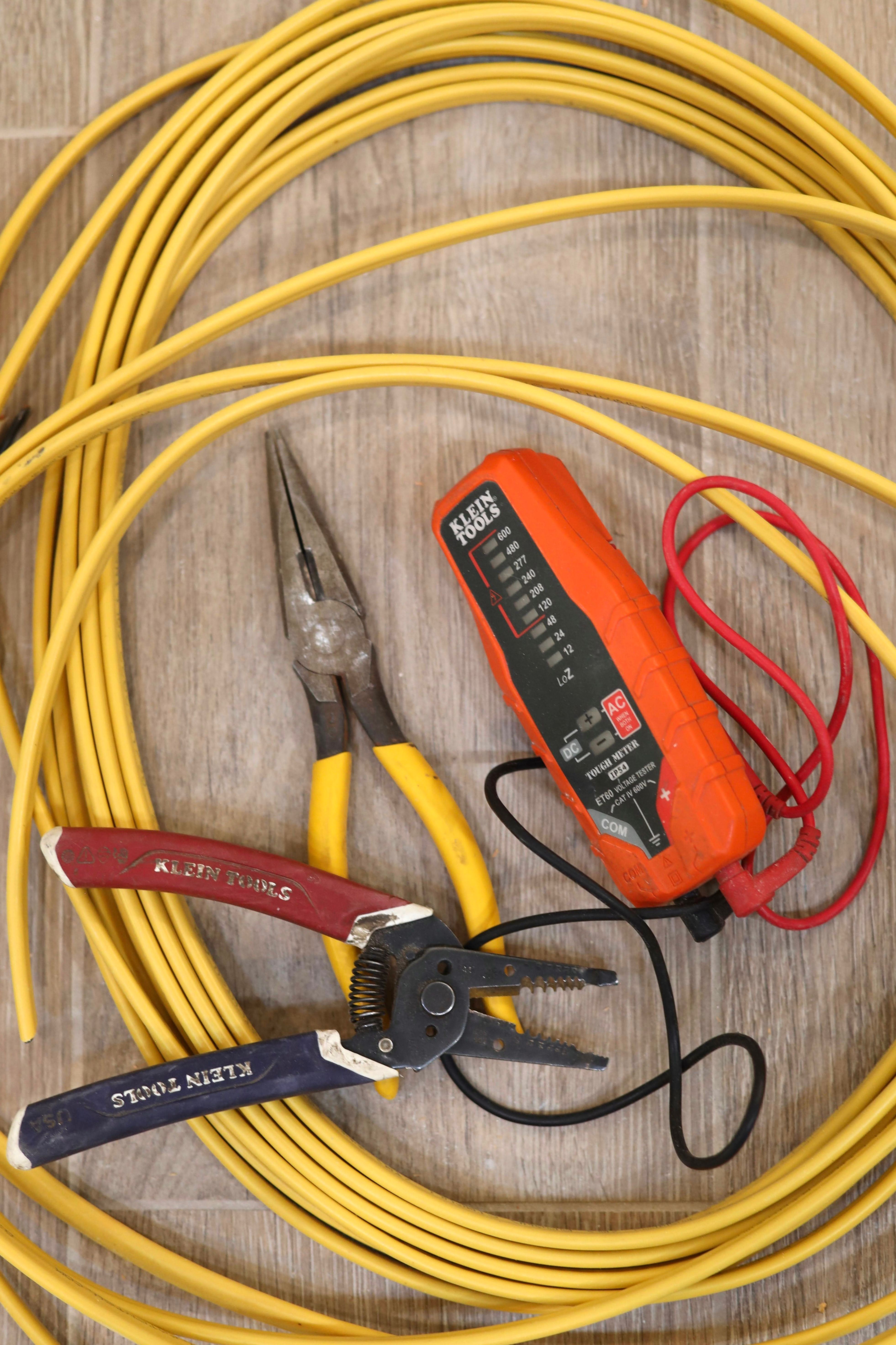 Pliers, wire strippers and a voltage tester on a coil of yellow wire