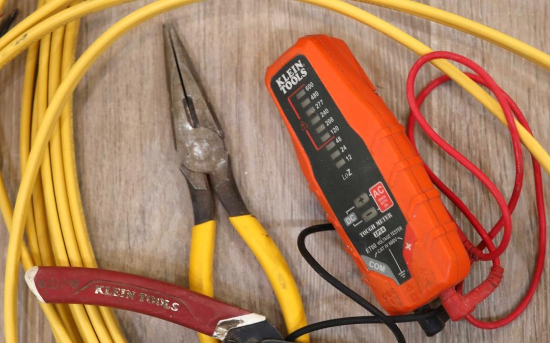 Pliers, wire strippers and a voltage tester on a coil of yellow wire