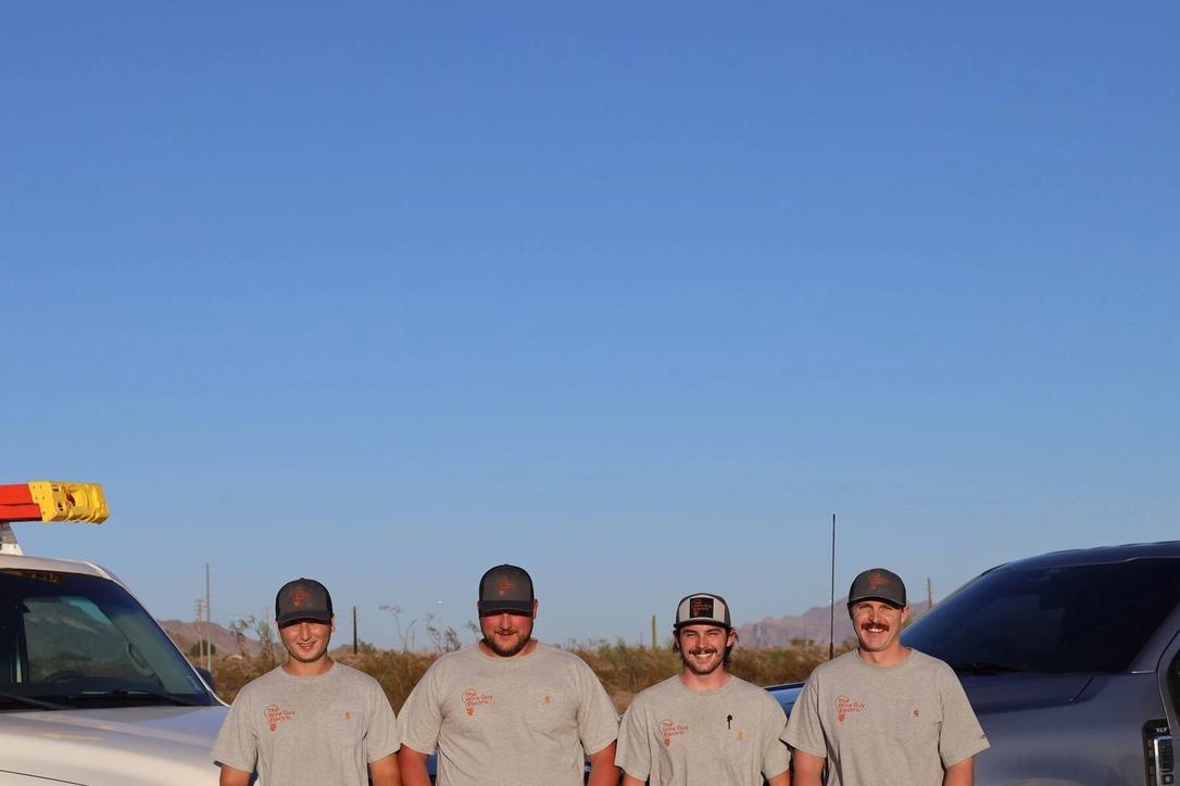 Four Wire Guy Electric technicians standing between a branded work van and pickup in the desert