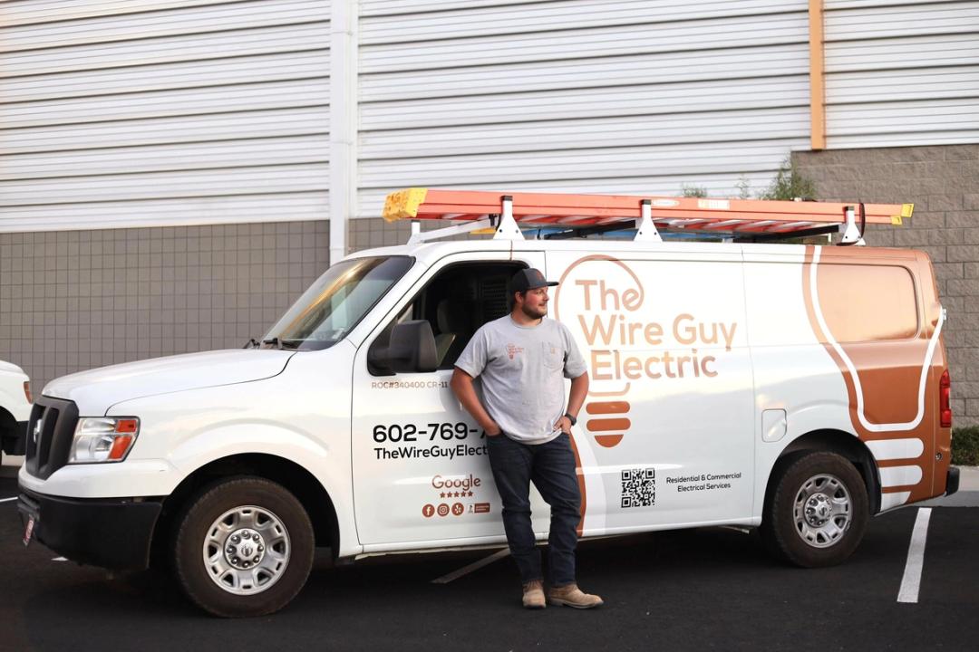 Electrician leaning against a Wire Guy Electric van with ladders on the roof
