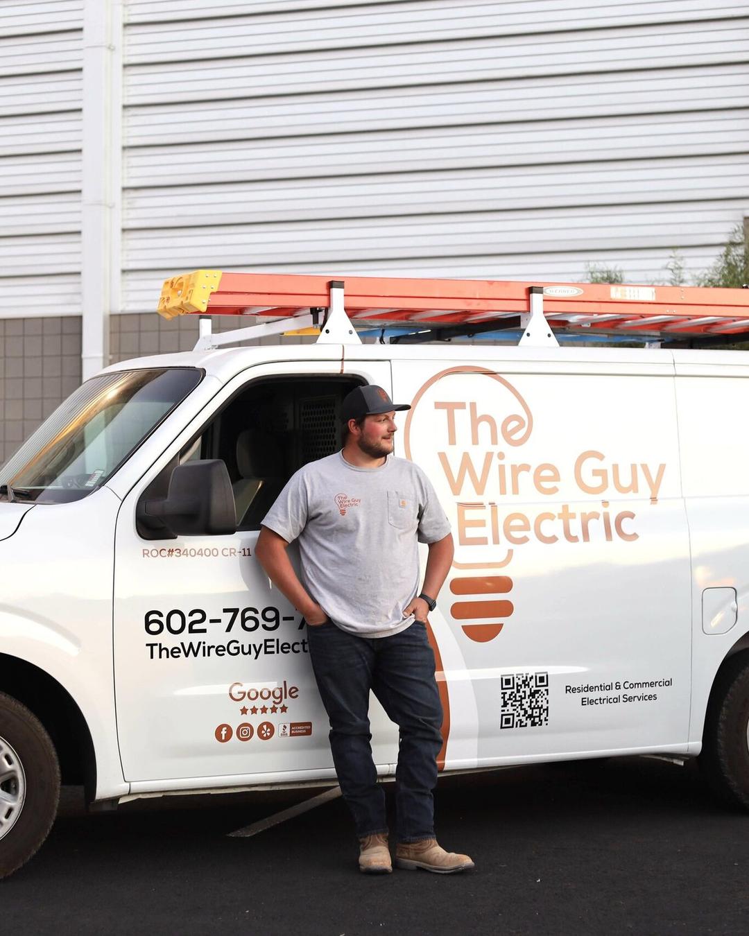Electrician leaning against a Wire Guy Electric van with ladders on the roof