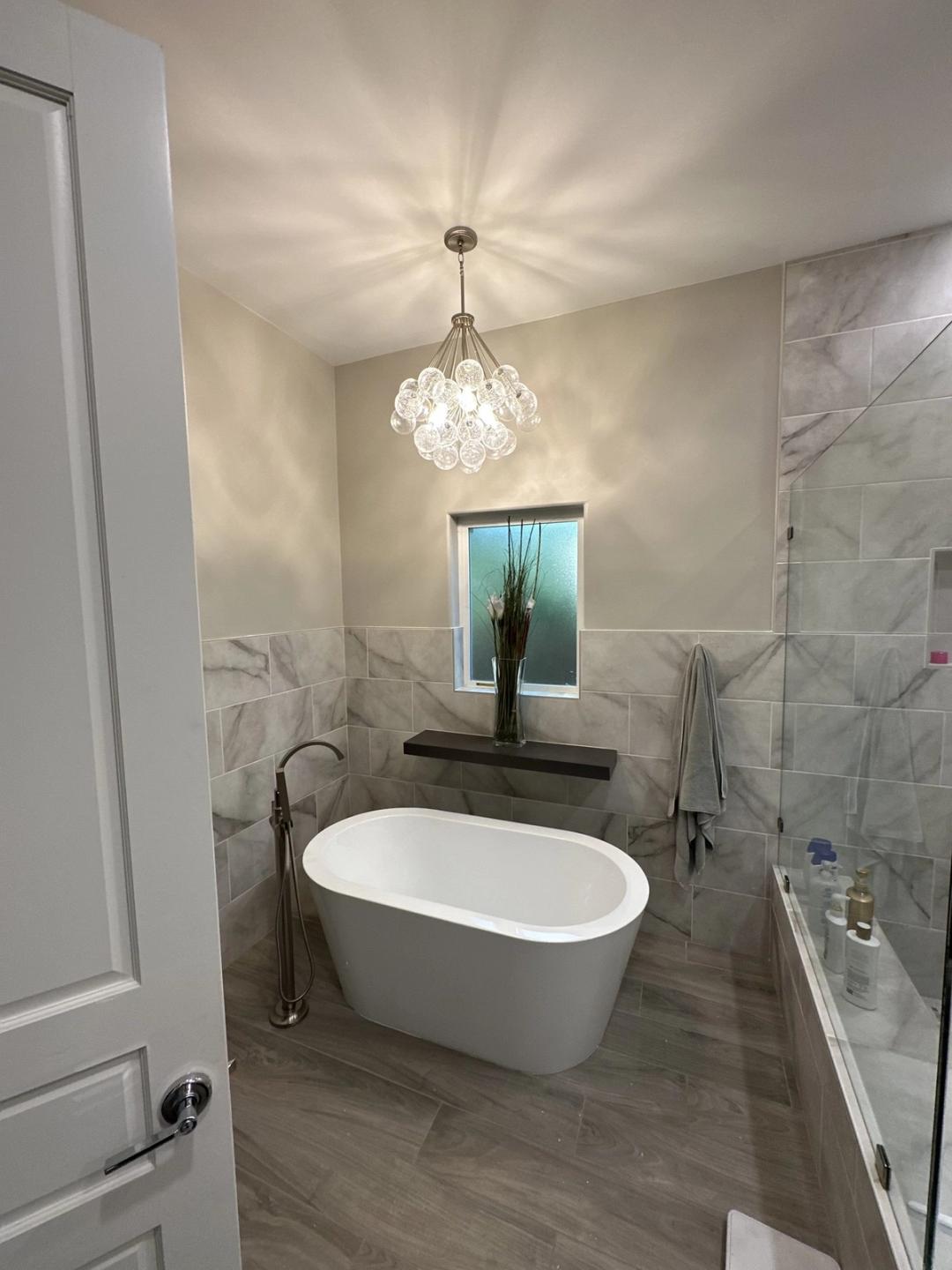 Glass bubble pendant hanging above a freestanding tub in a marble-tiled bathroom