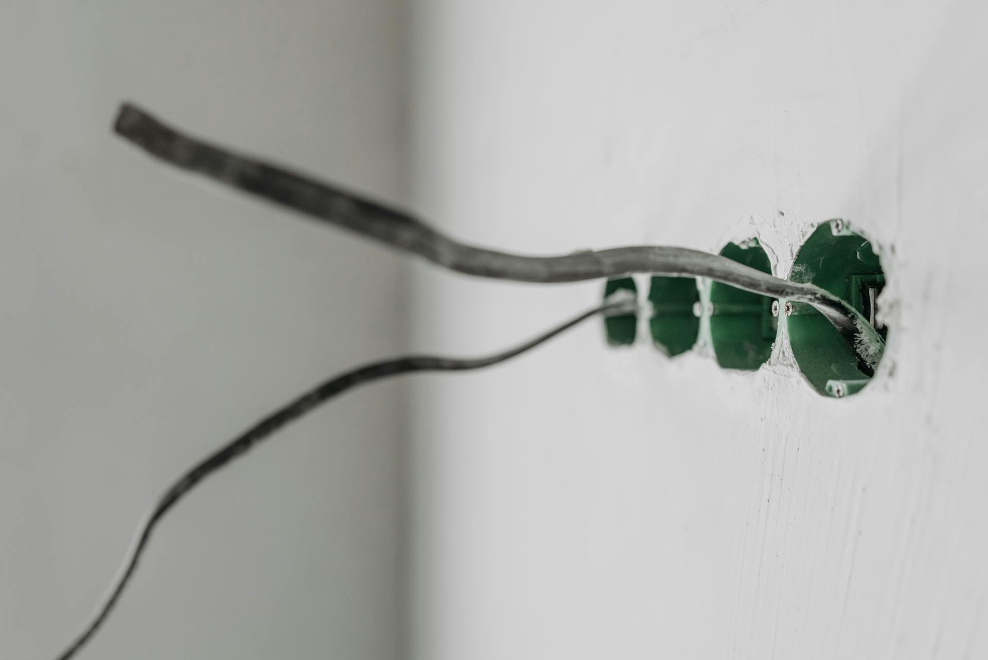 Old wires sticking out of open electrical boxes in a white wall