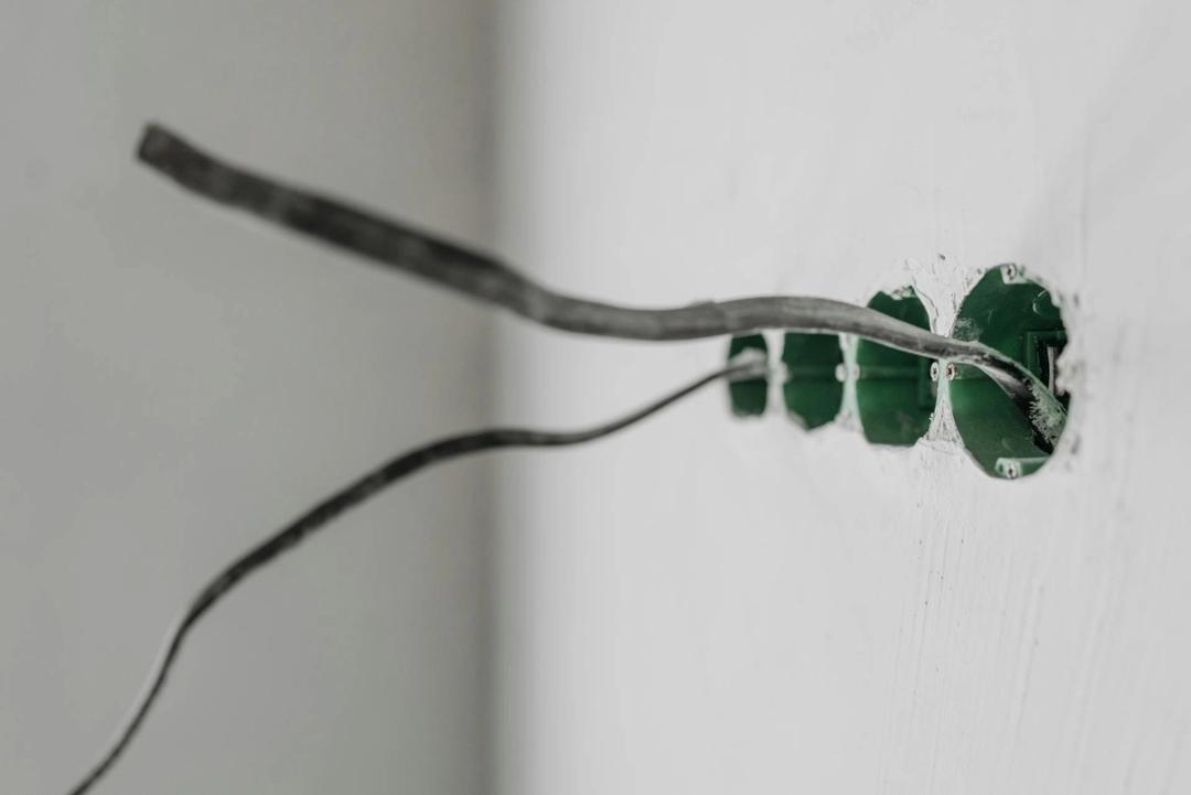 Old wires sticking out of open electrical boxes in a white wall