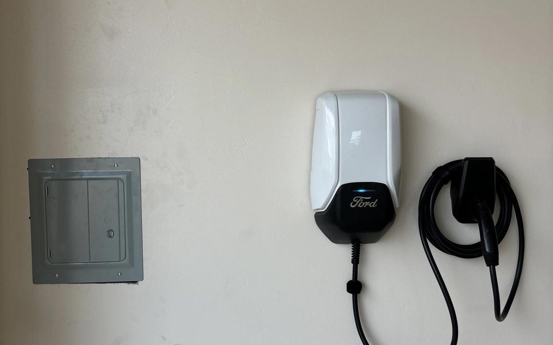 Ford wall-mounted EV charger with coiled cable next to a subpanel in a garage