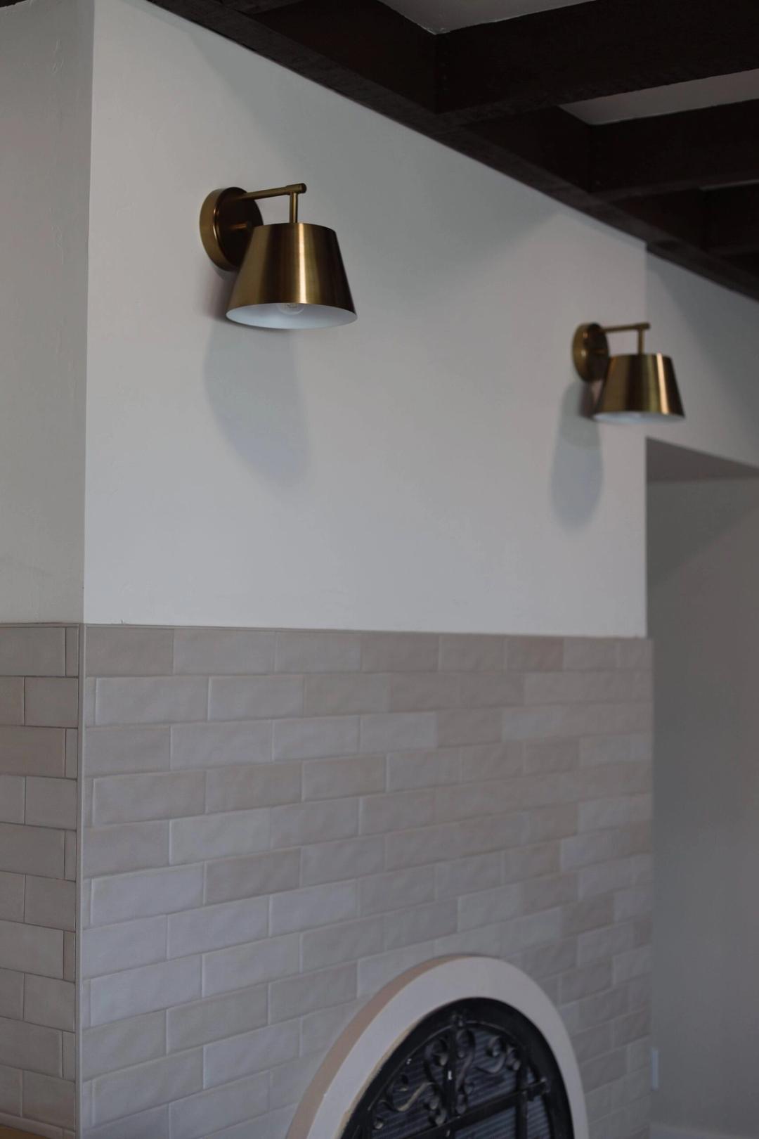Two brass wall sconces above a white tiled fireplace surround with an arched opening
