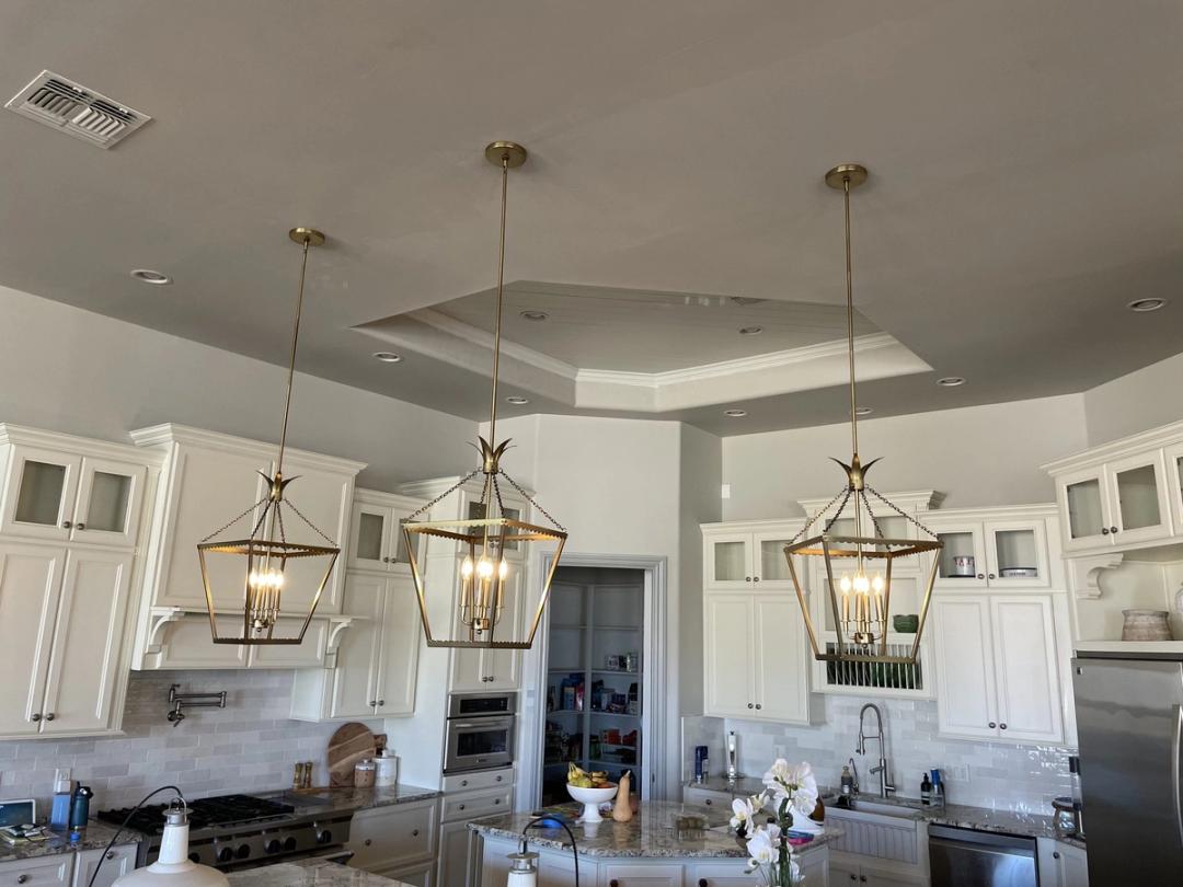 Three brass lantern pendants over an island in a white kitchen with a tray ceiling