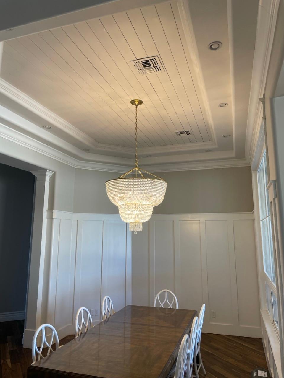 Chandelier hanging over a dining table in a room with a coffered ceiling and wainscoting