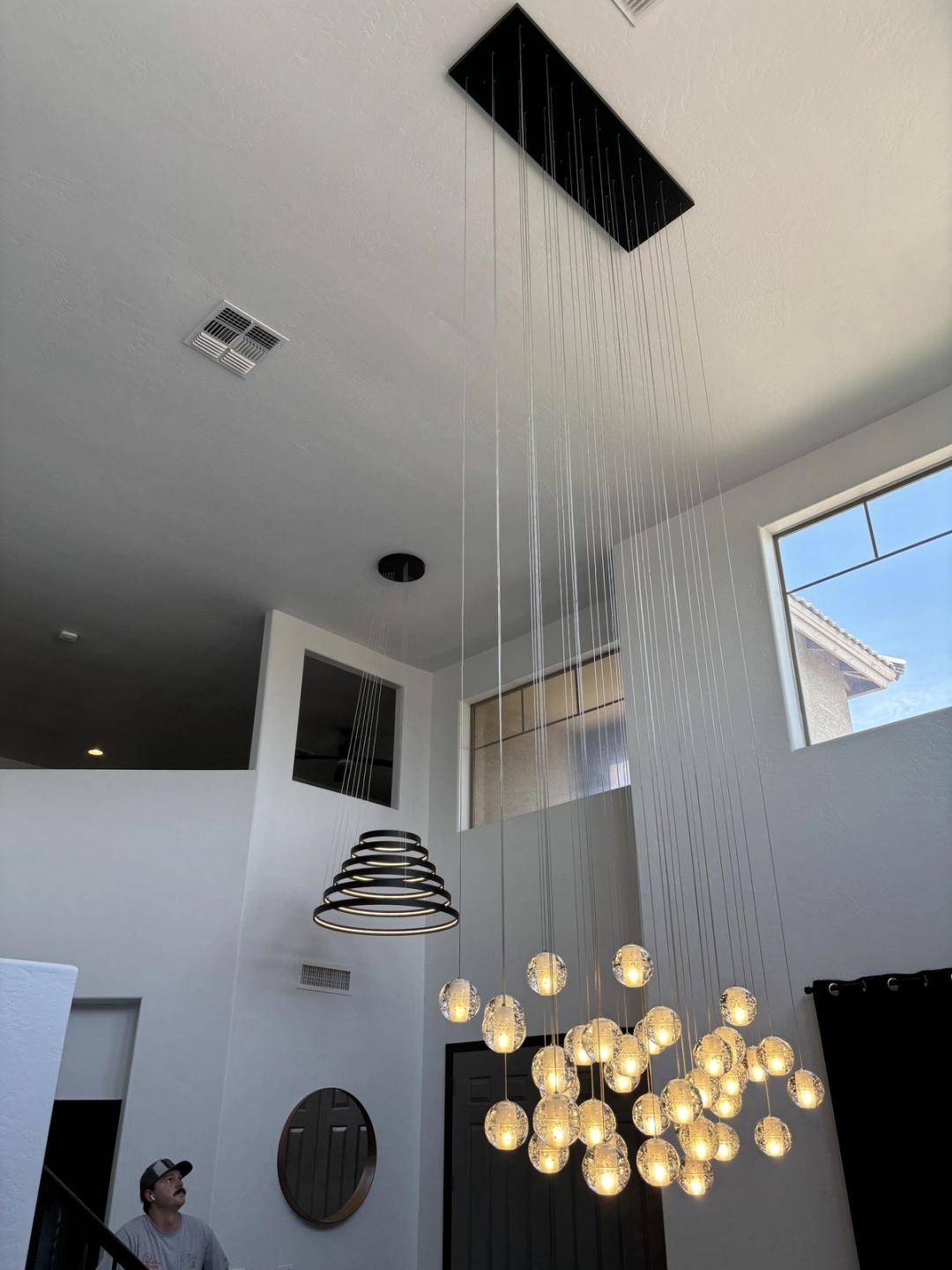 Glass bubble cluster chandelier and spiral pendant in a tall entry as an electrician looks up