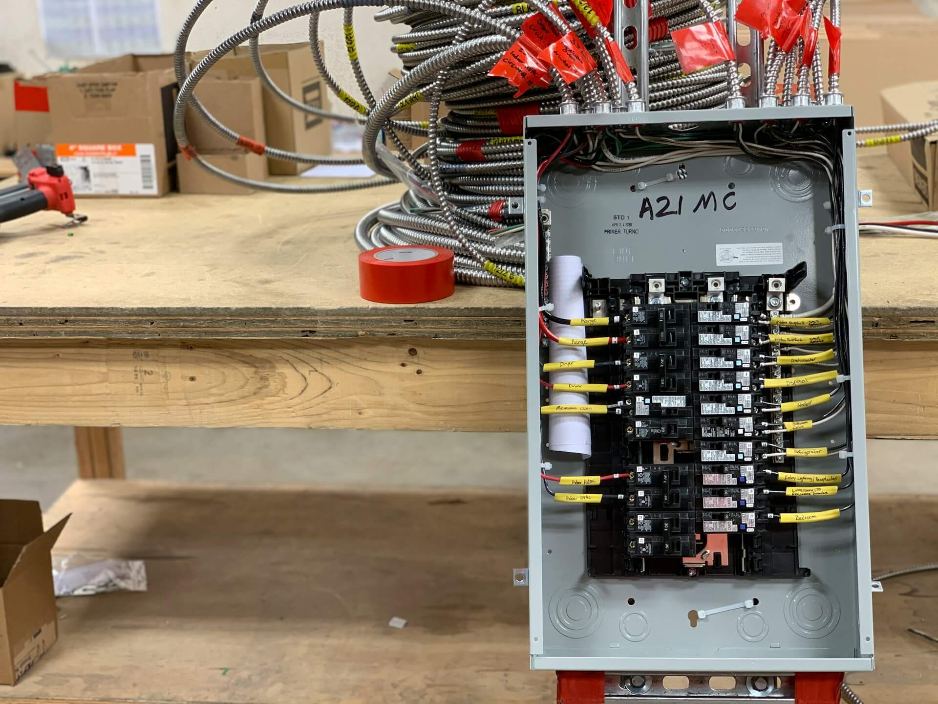A new breaker panel, wired and labeled, standing on a workbench beside coils of armored cable