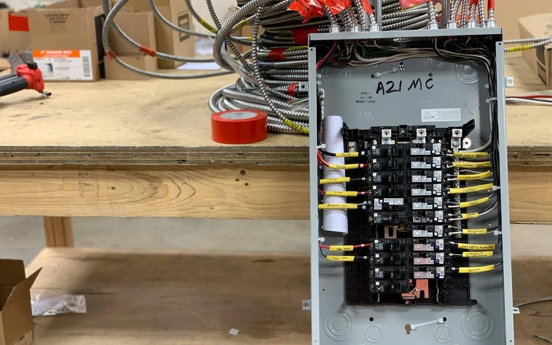 A new breaker panel, wired and labeled, standing on a workbench beside coils of armored cable