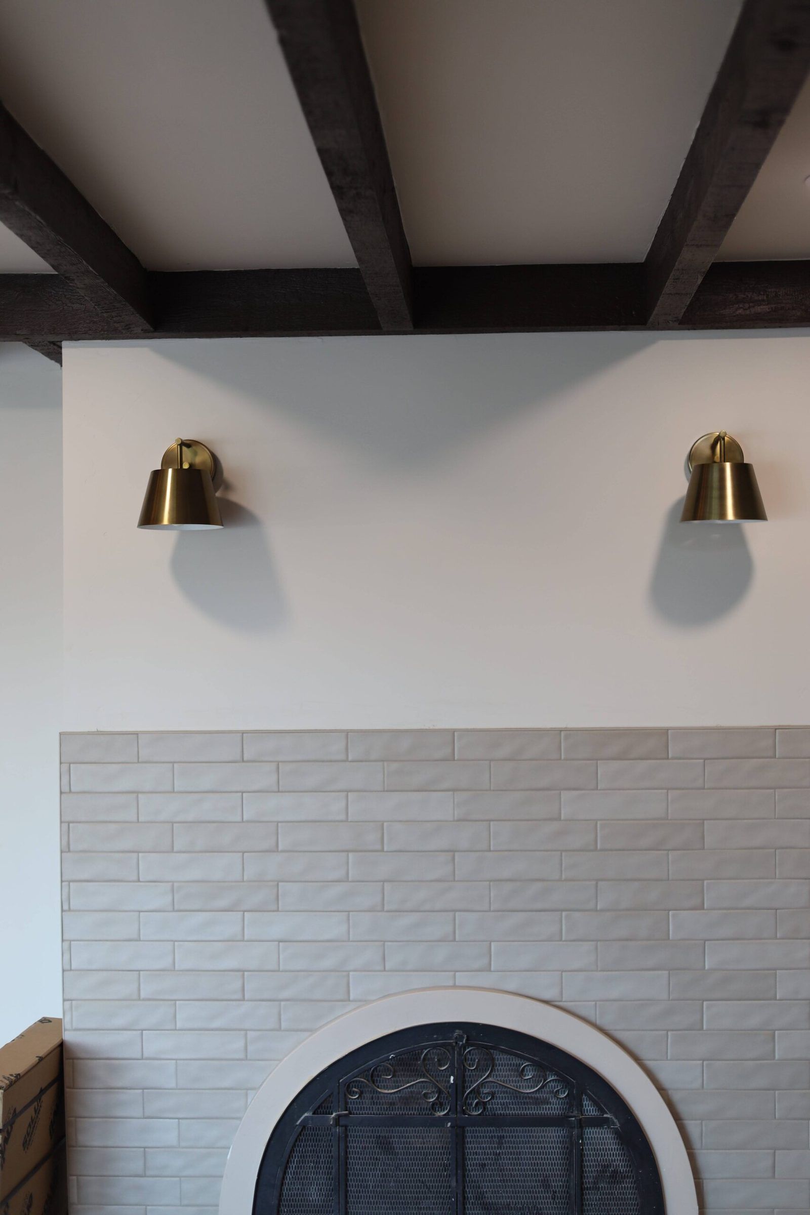 Two brass sconces above a white brick fireplace under wood beams
