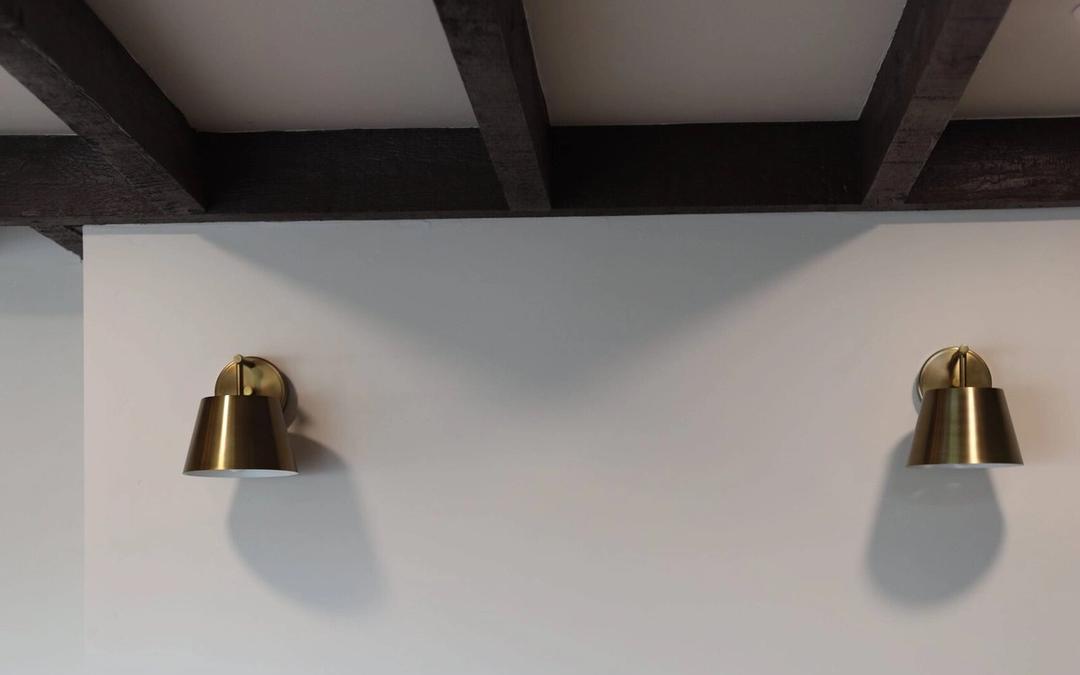 Two brass sconces above a white brick fireplace under wood beams