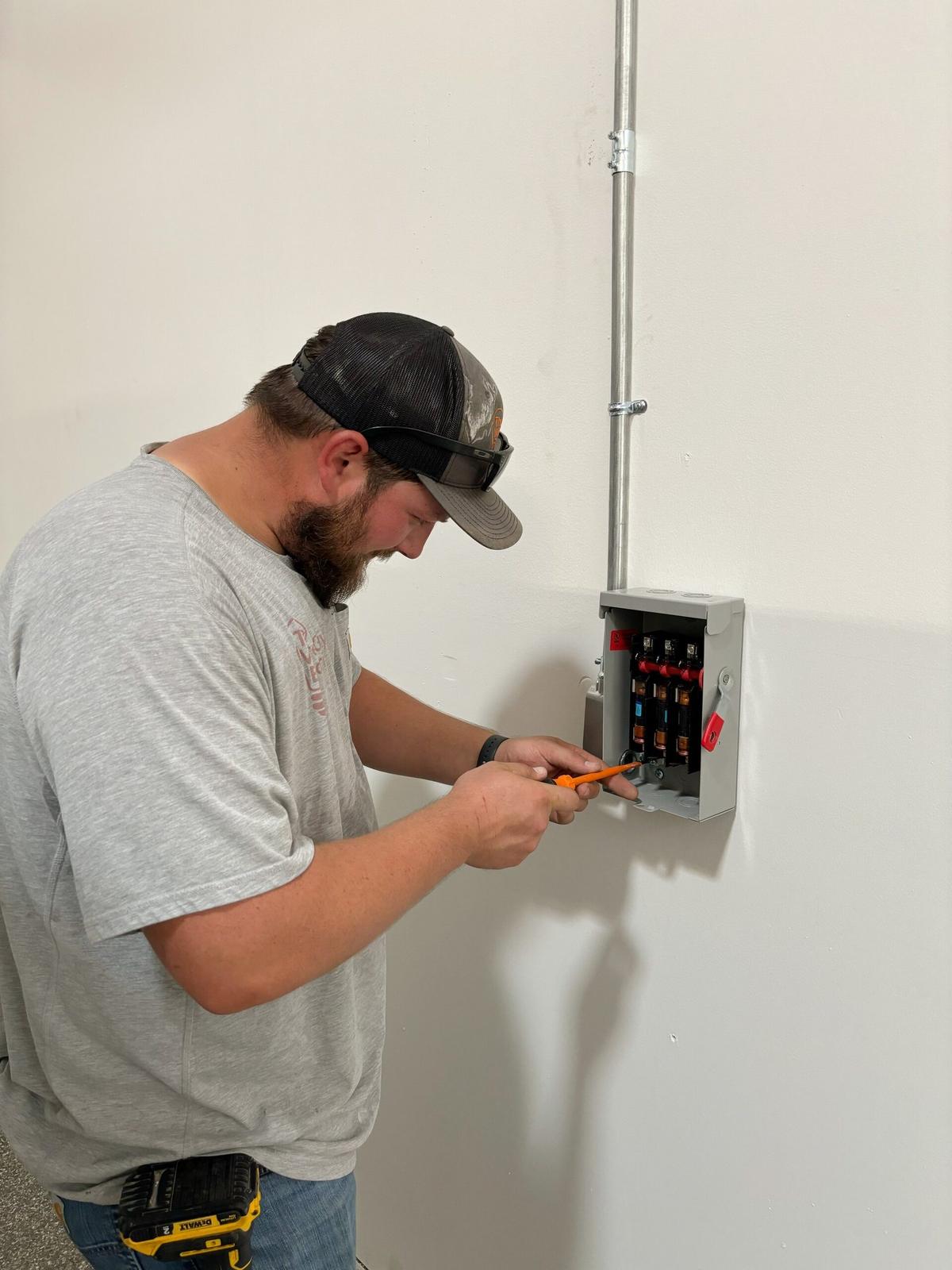 Bearded electrician wiring a fused disconnect switch on a white wall