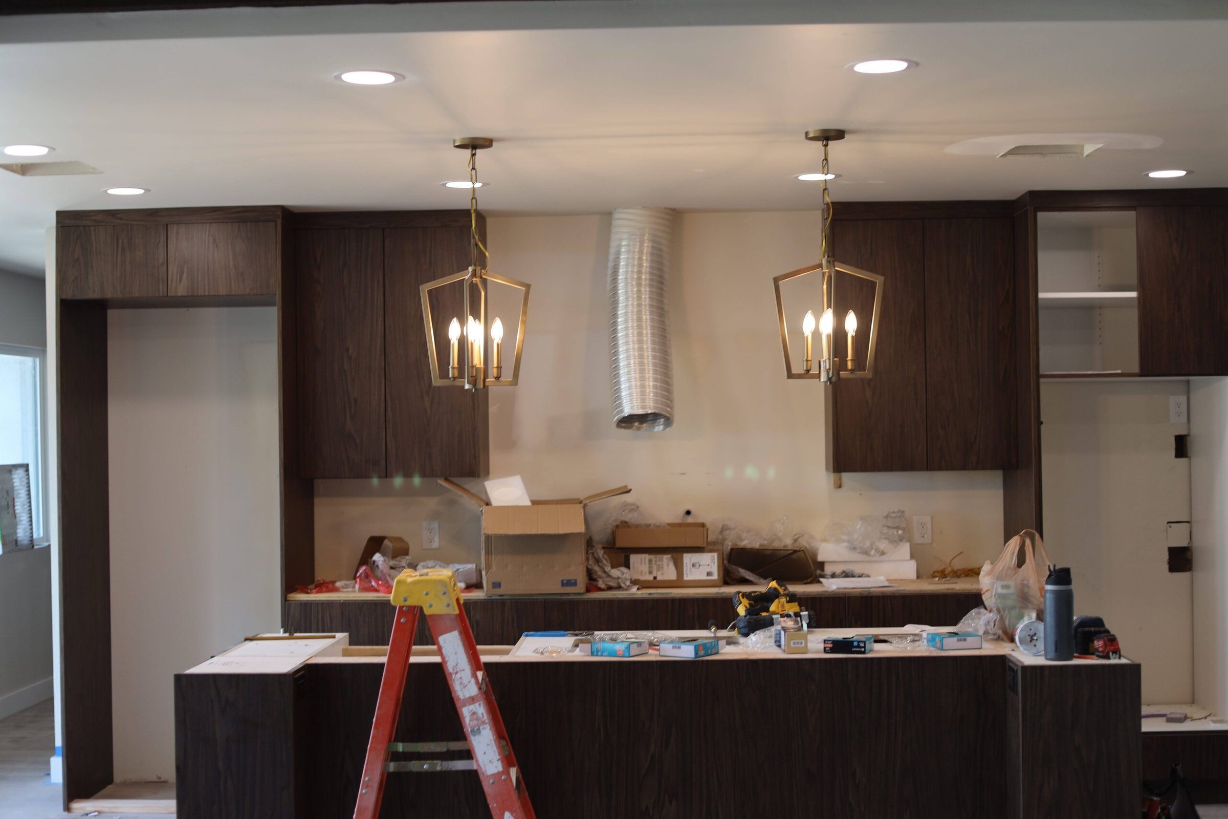 Two brass lantern pendants over a dark-wood kitchen island under construction, recessed lights above