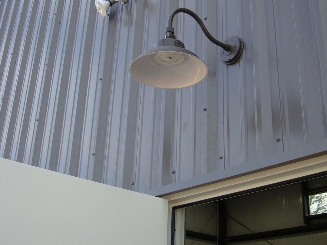 Black gooseneck barn light and floodlight on a gray metal building above a door