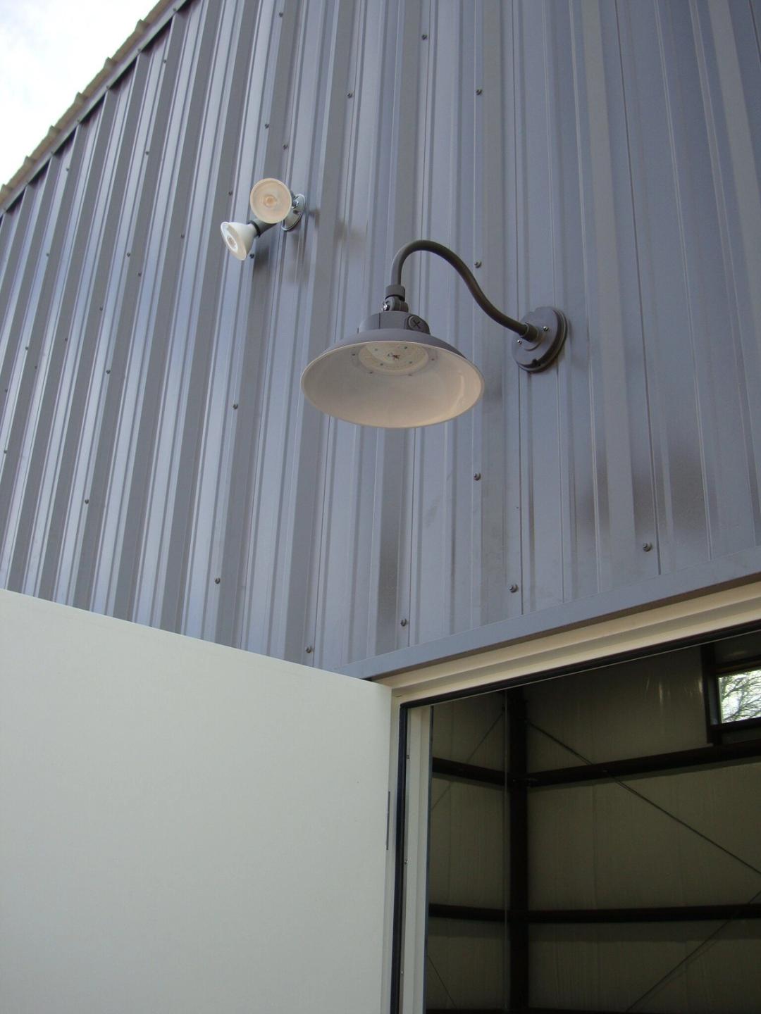 Black gooseneck barn light and floodlight on a gray metal building above a door