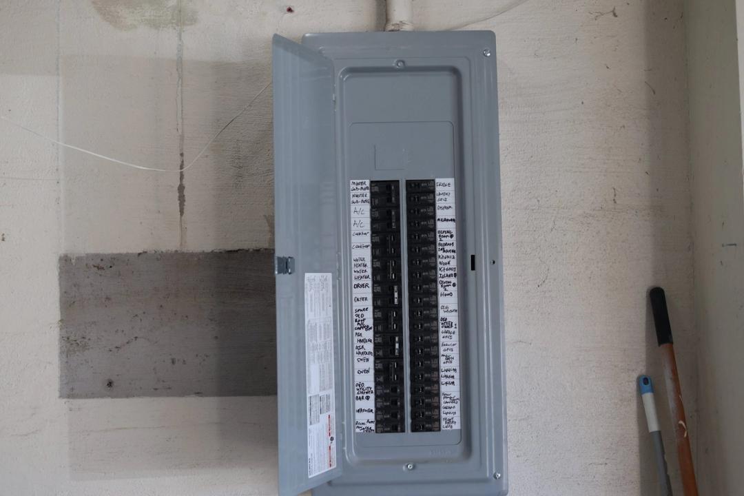 Electrical panel with door open and handwritten circuit directory on a concrete wall
