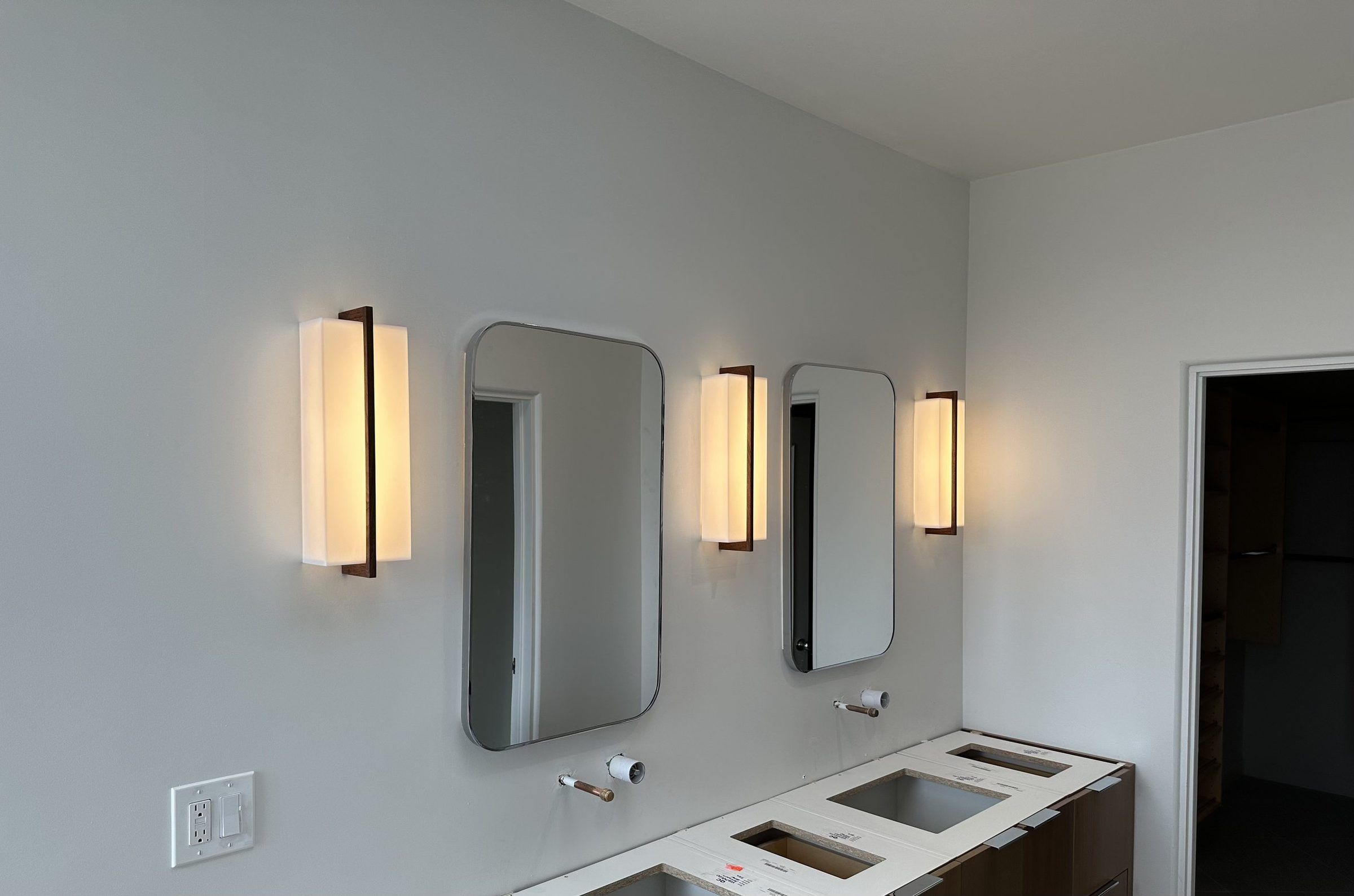 Three warm vertical wall sconces flanking mirrors above a new double bathroom vanity