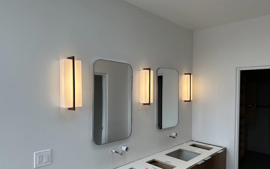 Three warm vertical wall sconces flanking mirrors above a new double bathroom vanity