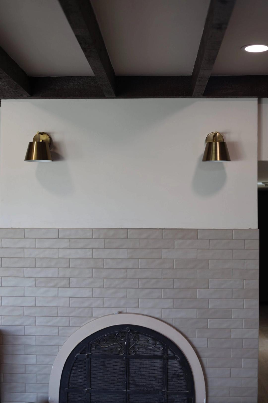 Pair of brass sconces above a white brick fireplace with beams overhead