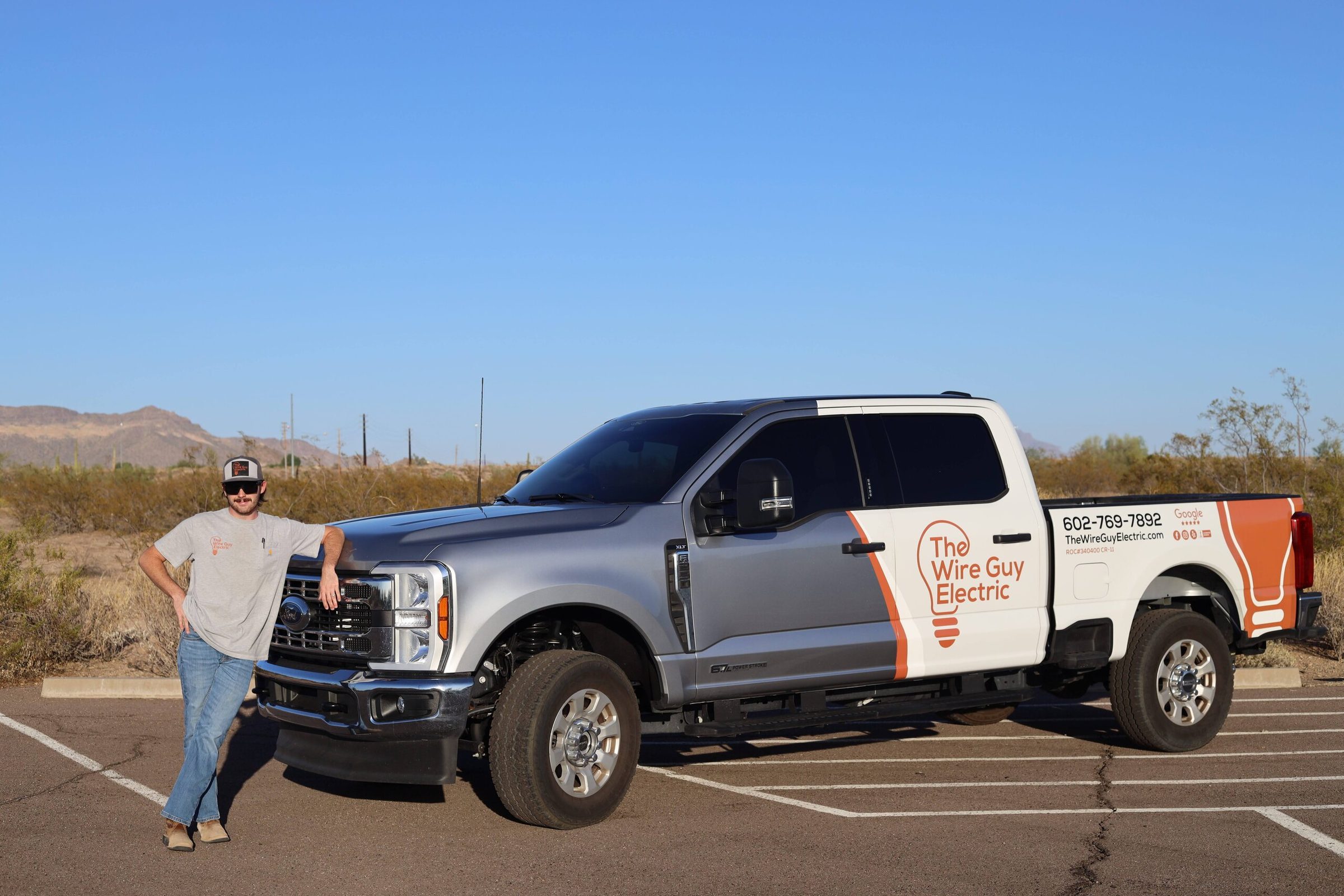 Wire Guy Electric technician in sunglasses leaning on a branded silver and white pickup in the desert
