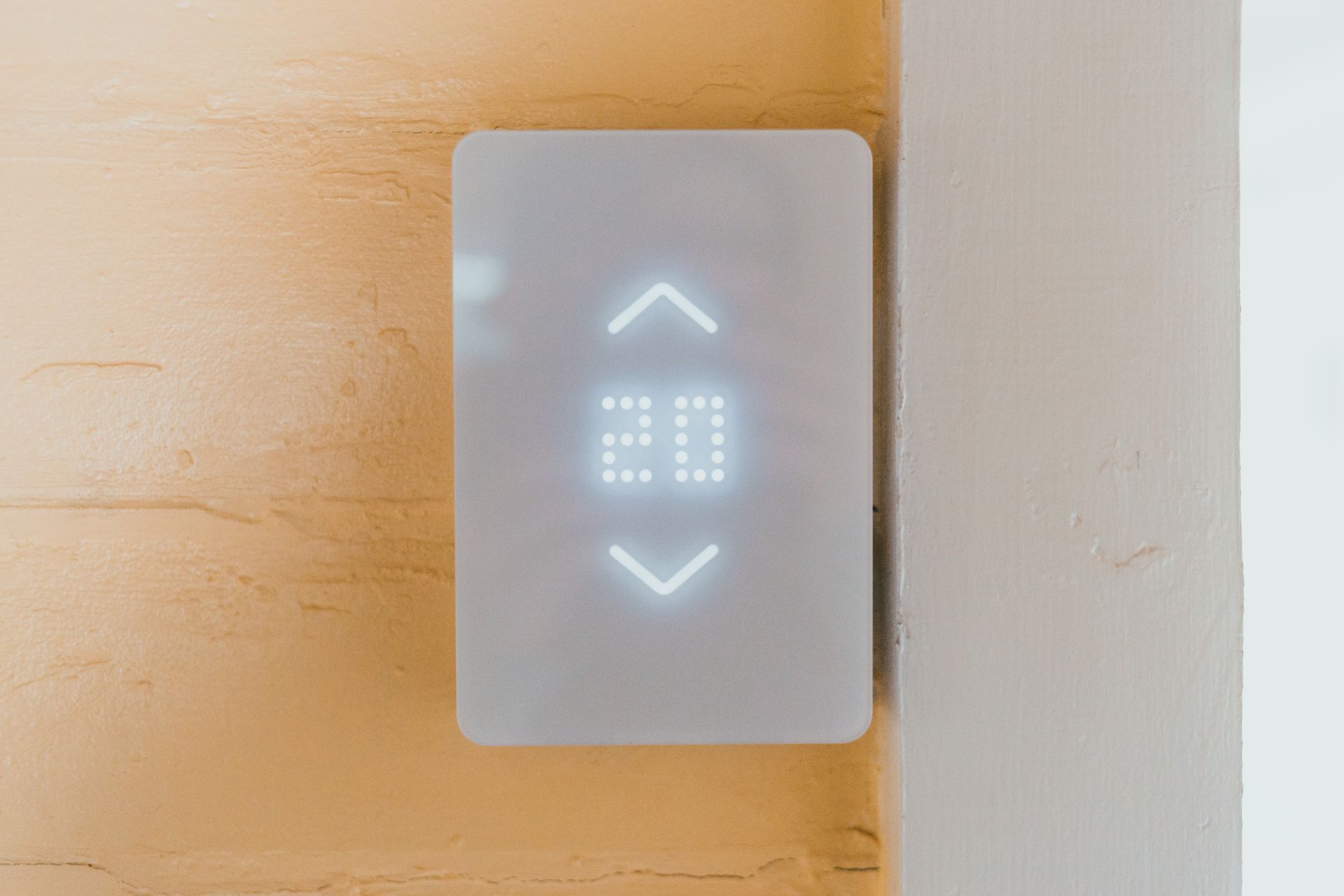A white smart thermostat with a lit display on a warm plaster wall
