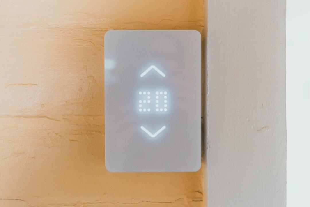 A white smart thermostat with a lit display on a warm plaster wall