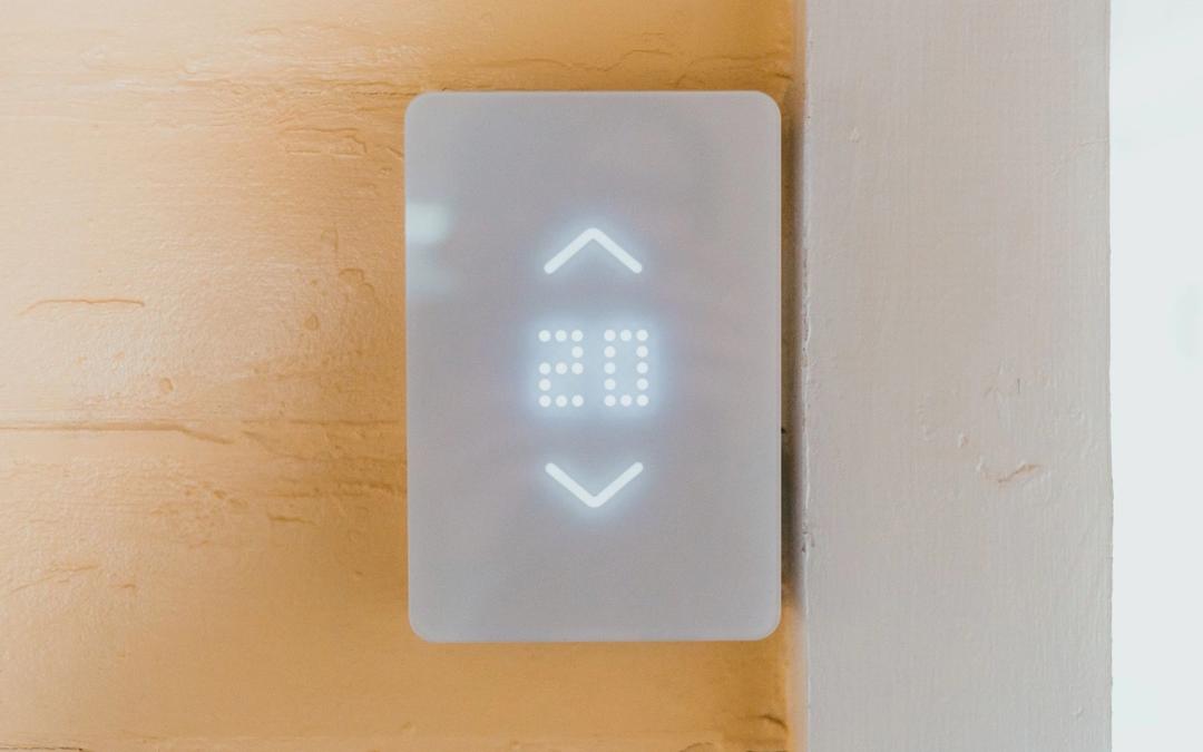 A white smart thermostat with a lit display on a warm plaster wall