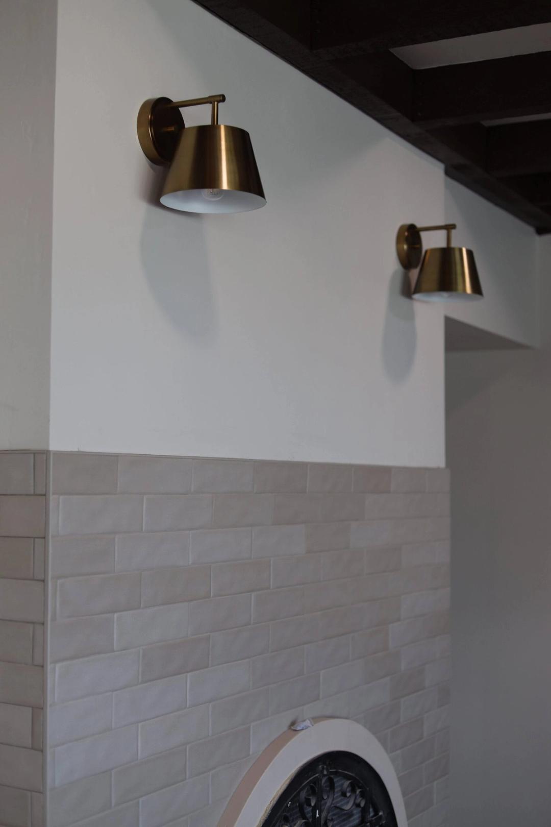 Brass sconces on a white wall above a tile wainscot