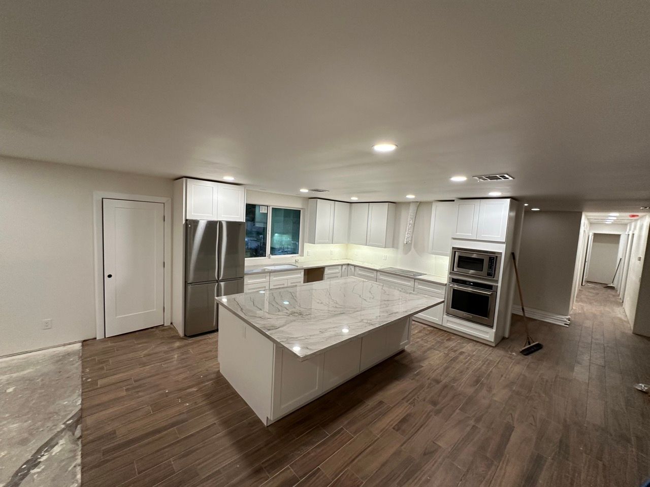 A finished kitchen remodel with recessed lights, white cabinets and a stone island