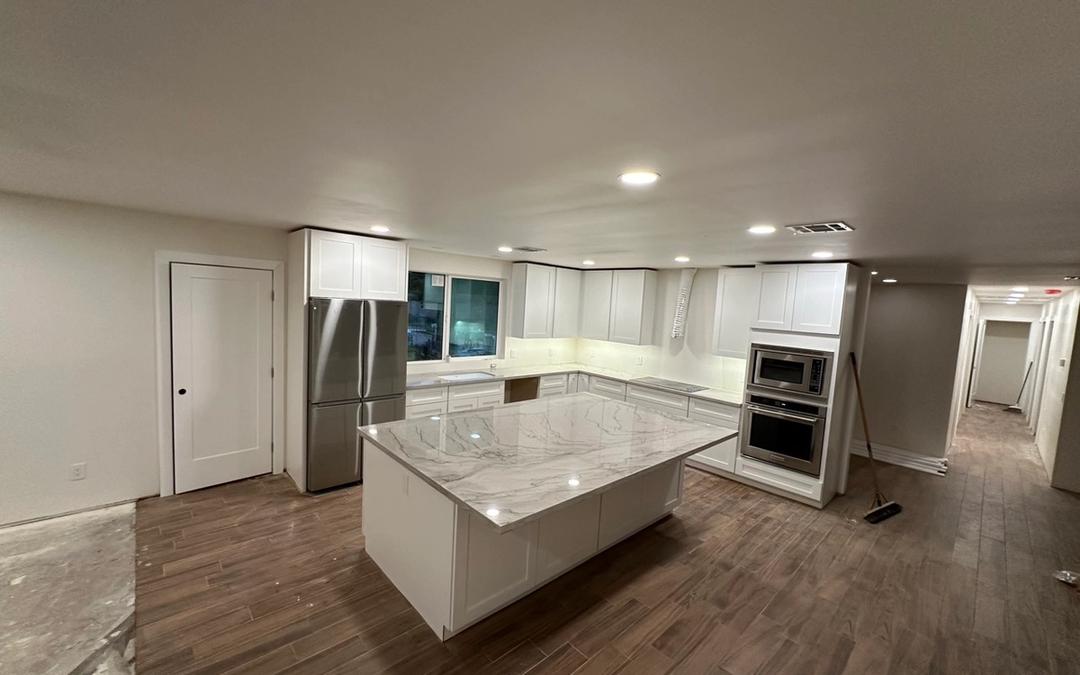 A finished kitchen remodel with recessed lights, white cabinets and a stone island