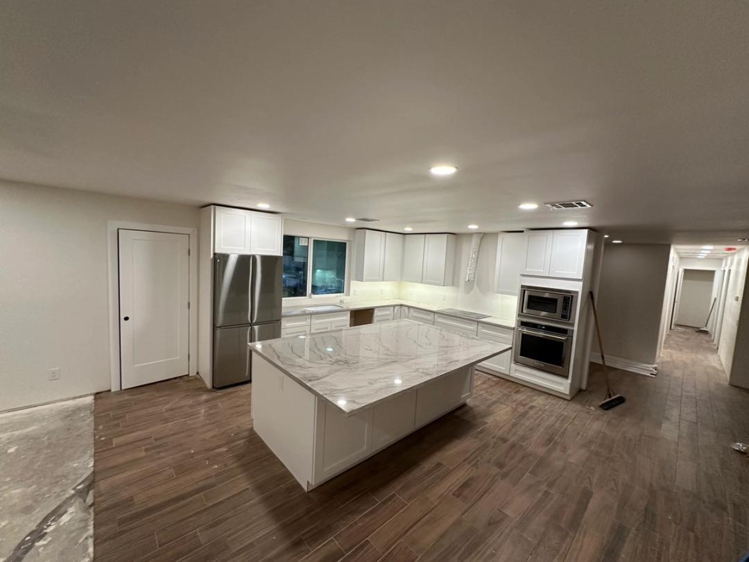 A finished kitchen remodel with recessed lights, white cabinets and a stone island