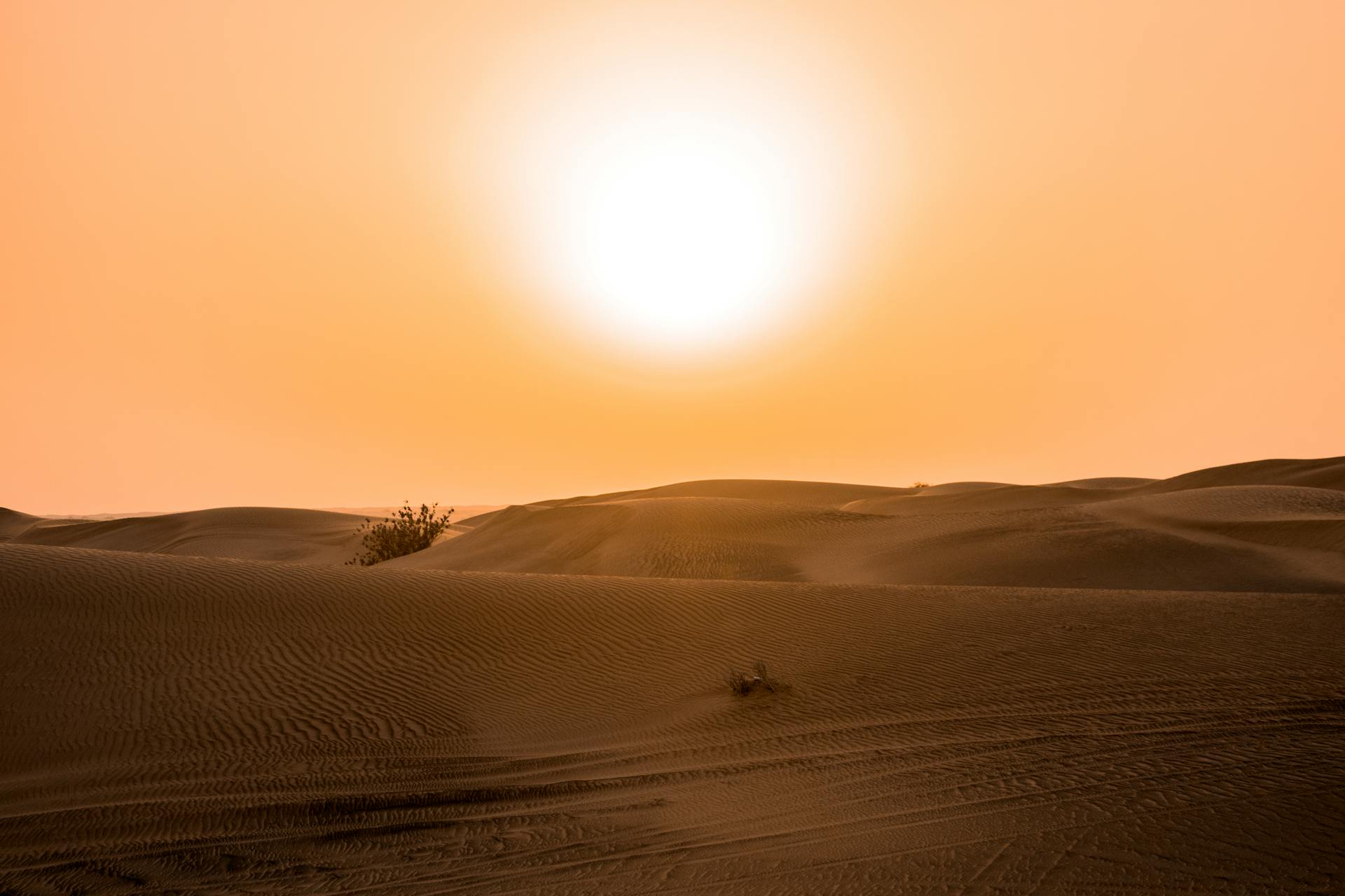 The sun blazing over desert sand dunes in an orange sky