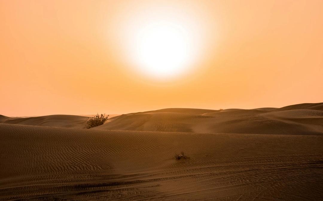 The sun blazing over desert sand dunes in an orange sky