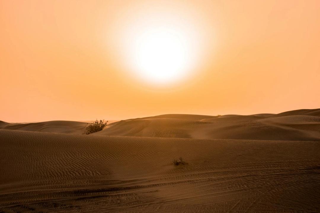 The sun blazing over desert sand dunes in an orange sky