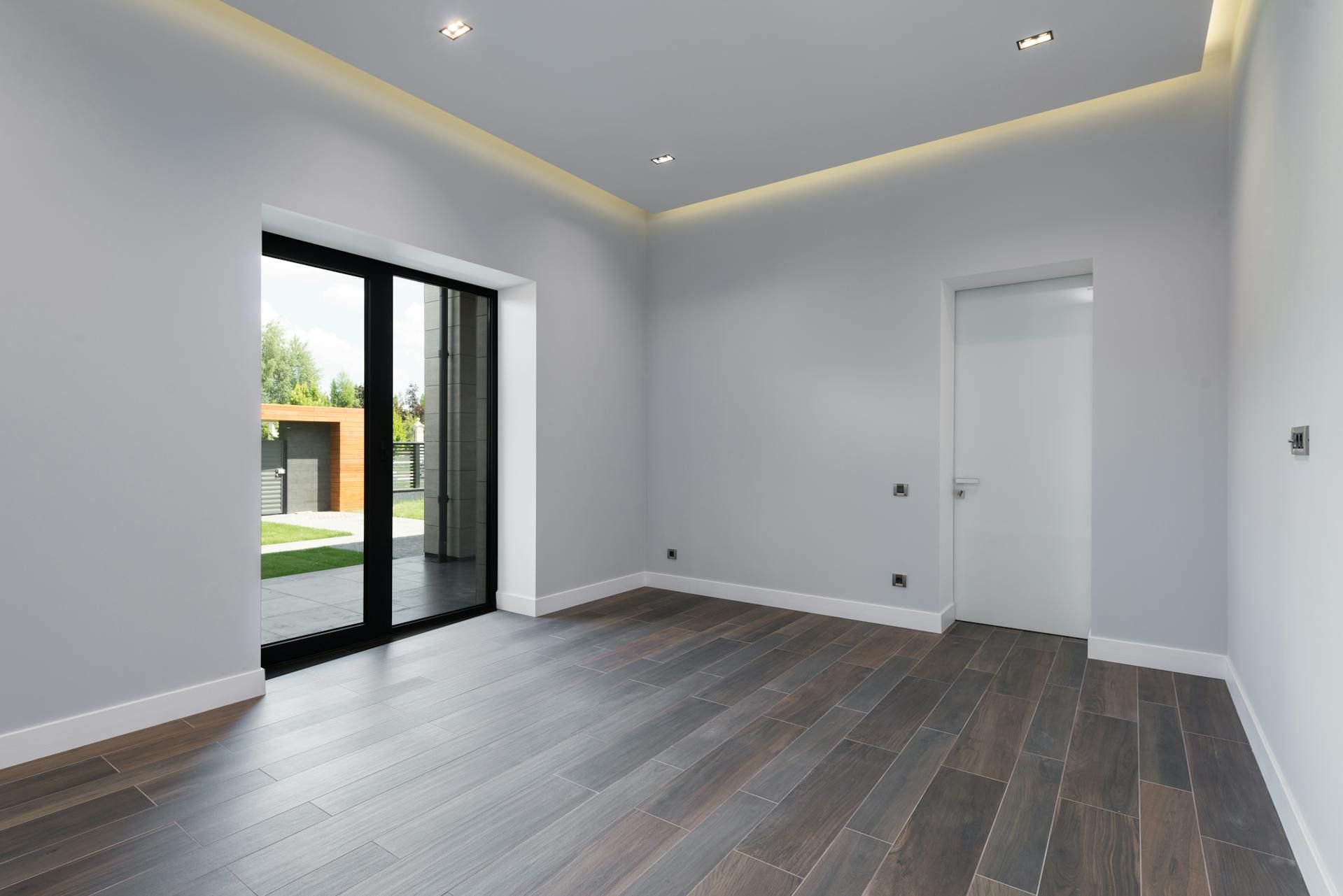 An empty modern room with recessed ceiling lights, a glowing ceiling cove and a glass door