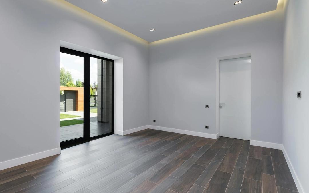 An empty modern room with recessed ceiling lights, a glowing ceiling cove and a glass door