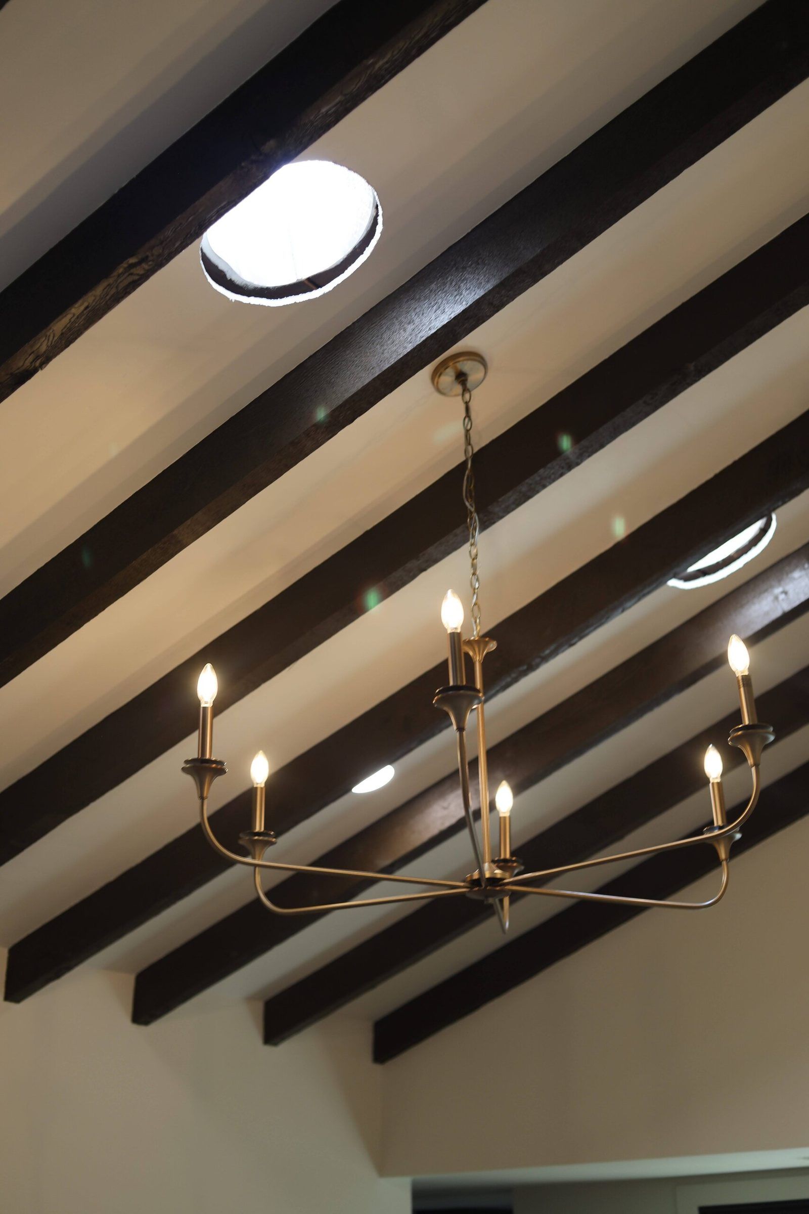 Lit brass candle chandelier under a sloped beamed ceiling